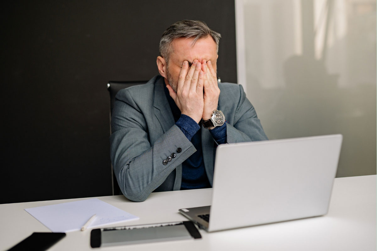 IT director stressed over rising multi-site rollout costs while working at laptop