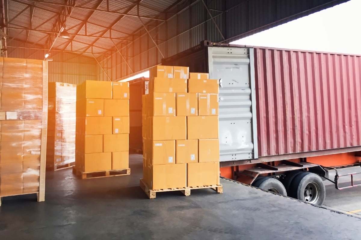 Pallets of IT equipment staged in a warehouse next to a shipping container, ready for distribution to multiple business locations
