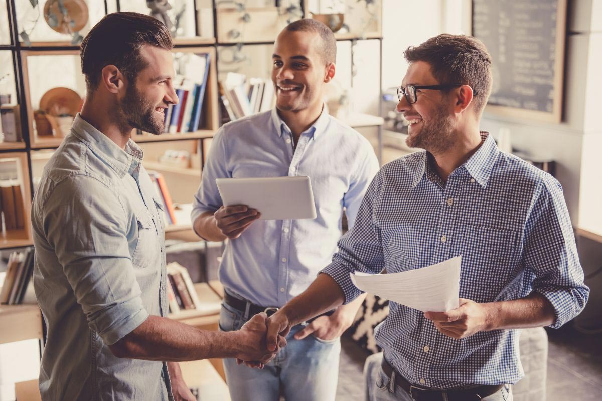 Three professionals meeting in an office and shaking hands to represent the partnership between Vetcor and MellinTech on multi-site technology projects